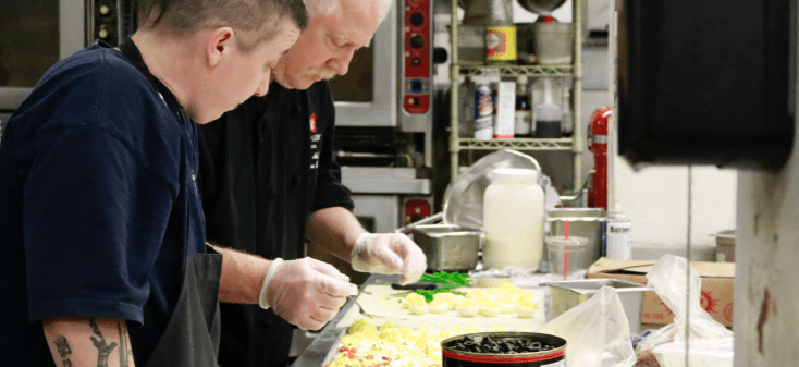 Image: a Chef trains a new employee on how to cook in a kitchen.