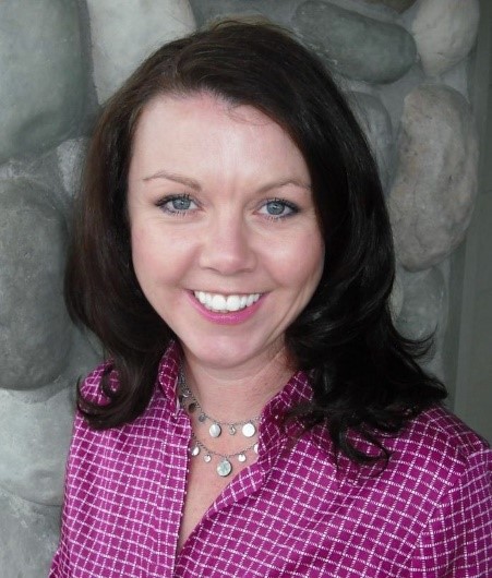 Image: Val Morgan, a white woman with dark brown hair and a purple shirt smiles.