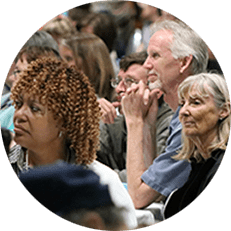 Image: Circular photo of people listening in a crowded conference room.