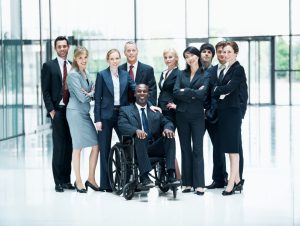 Image: Group of businesspeople standing around their colleague sitting in a wheelchair while smiling