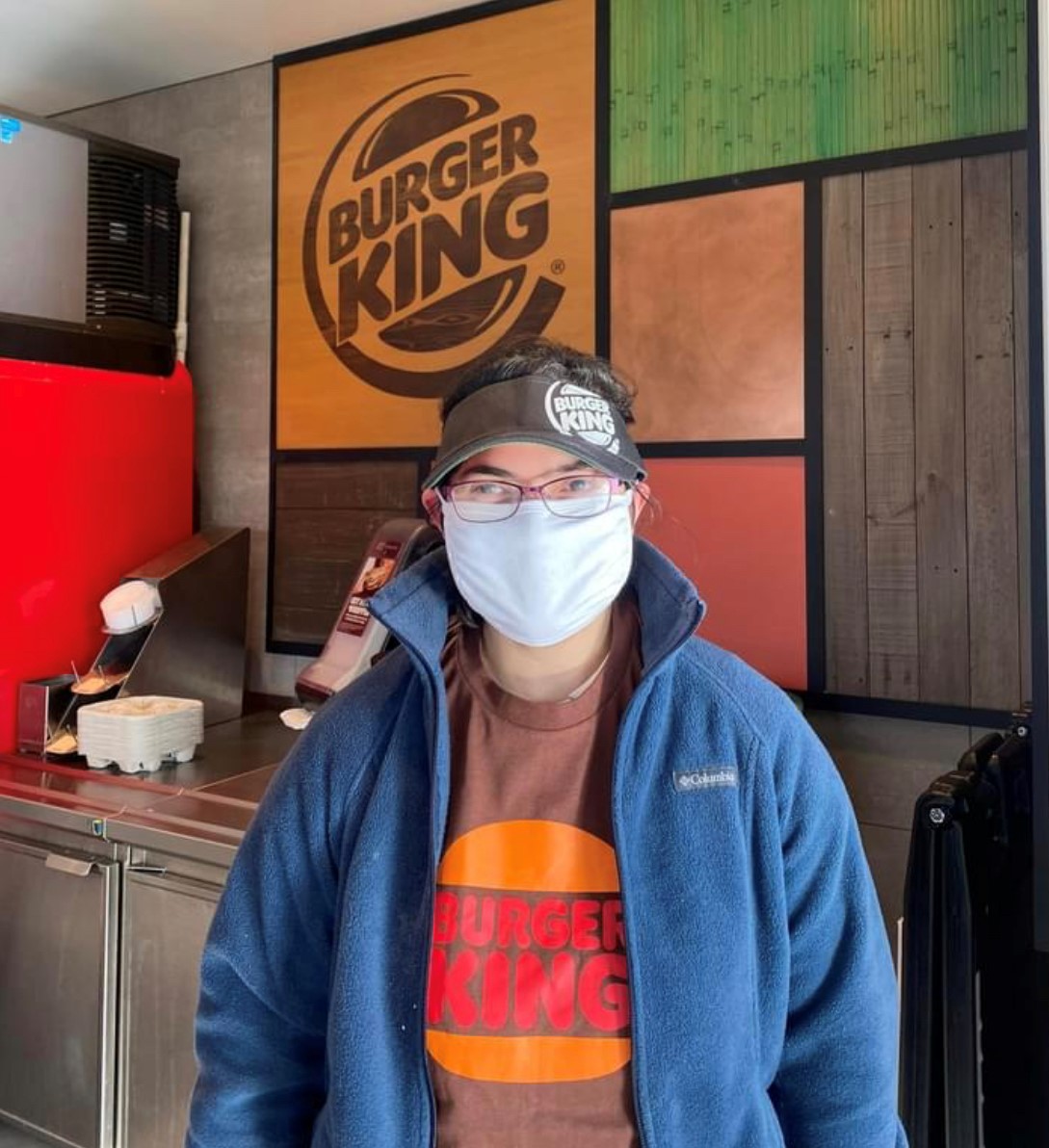 Image: Burger King worker wearing a BK visor, shirt, and blue fleece jacket. Photo is waist up.