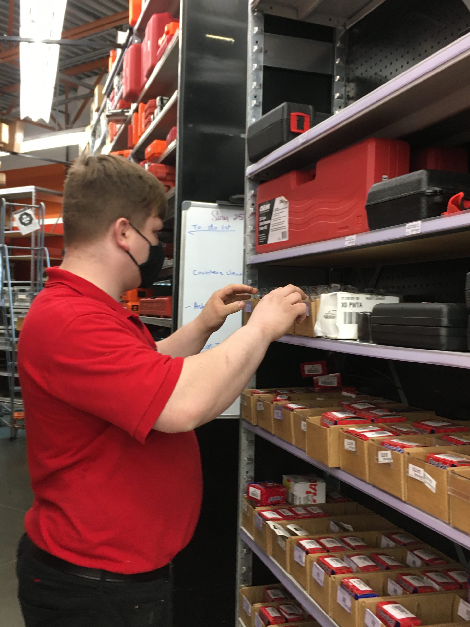 Image: Man with brown hair and red shirt looks for an automotive part on the shelf at Autozone. Profile view.