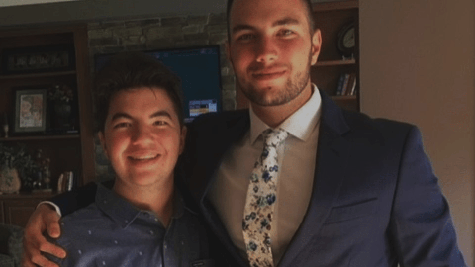 Image: photo of two men smiling. The taller man stands on the right with his arm around the shorrter man.
