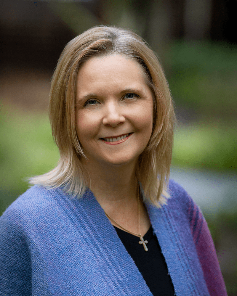 Image: Anne-Marie Lake, a white woman with brown hair and a blue cardigan smiles.