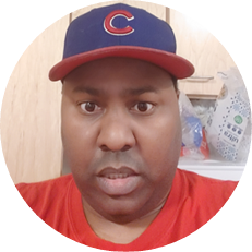 Image: Curtis Harris, a black man with a red shirt and a red and blue Chicago Cubs baseball cap.