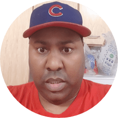 Image: Curtis Harris, a black man with a red shirt and a red and blue Chicago Cubs baseball cap.