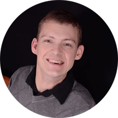 Photograph: Circular headshot of Wise Associate, Daman Wandke. Daman a white man with short, light brown hair. Daman is smiling and leaning forward, wearing a gray sweater with a black-collared shirt under it.