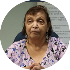 Image: Faith Chaufty, a black woman with long hair wearing a patterned purple blouse and folding her hands.