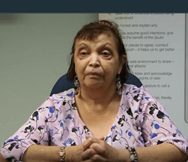 Image: Faith Chaufty, a black woman with long hair wearing a patterned purple blouse and folding her hands.