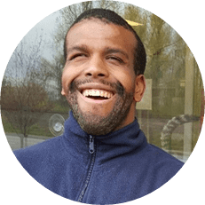 Image: Lance Wolcott, a black man with short black hair and short beard wearing a navy blue fleece jacket smiles