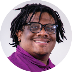 Image: Timothy Gordon Jr, a black man with dark-rimmed glasses and short dred locked hair smiles.