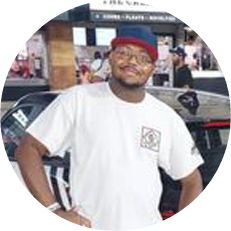 Image: William Bedford, a black man wearing glasses, a blue and red baseball hat and white t-shirt. Hands on hips, smiling.