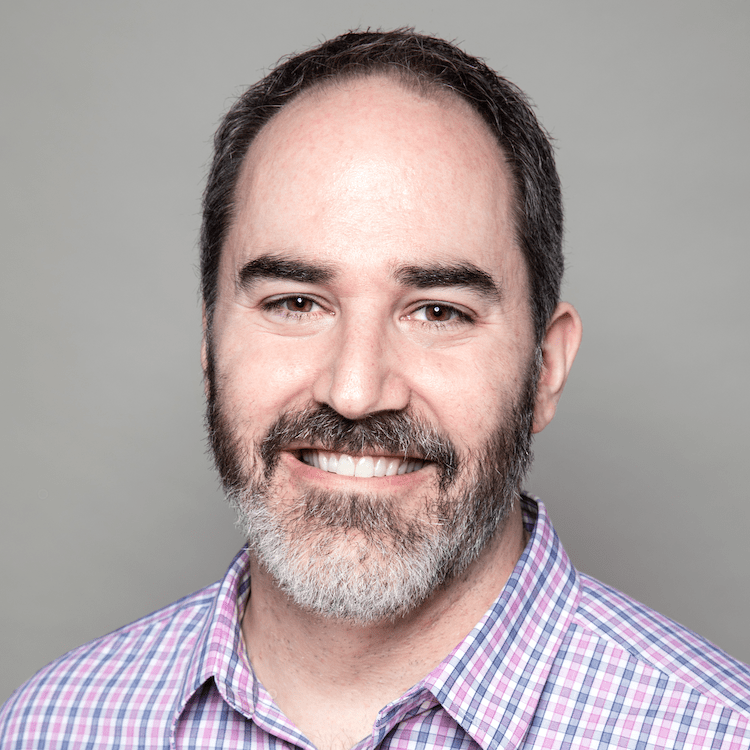 Image: Headshot of Jeff Akin, a white man with dark hair, receding hairline, salt and pepper beard wearing a blue and pink plaid shirt and smiling.