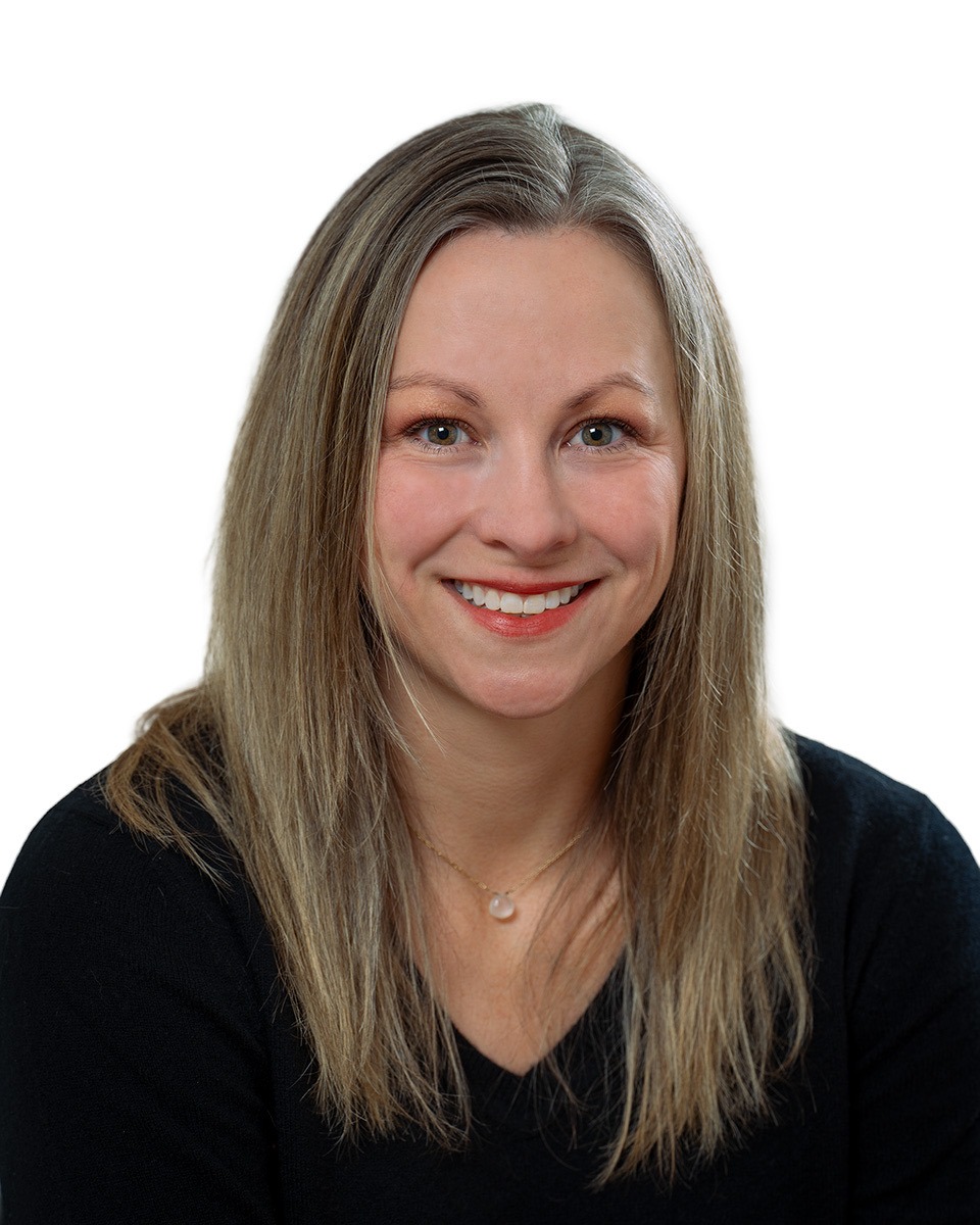 Image: Smiling woman with long brown hair, dressed in a black top against a white background.